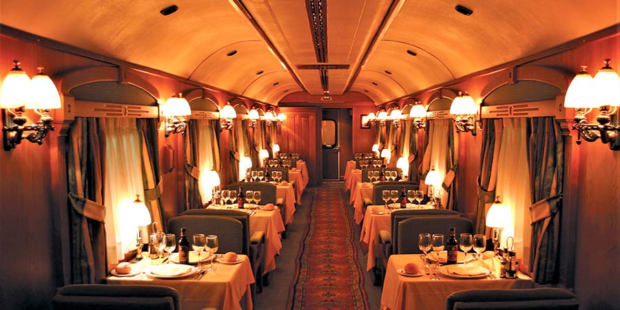 The dining car of La Costa Verde Express is lit by warm light and all tables are dressed for the evening meal. 